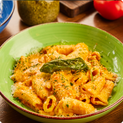 Bowl of rigatoni pasta with creamy tomato sauce, garnished with basil and grated parmesan cheese at Mangiare