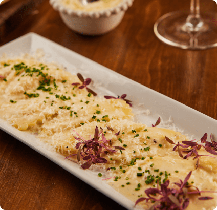 Plate of creamy ravioli topped with parmesan cheese and garnished with chives and microgreens at Mangiare